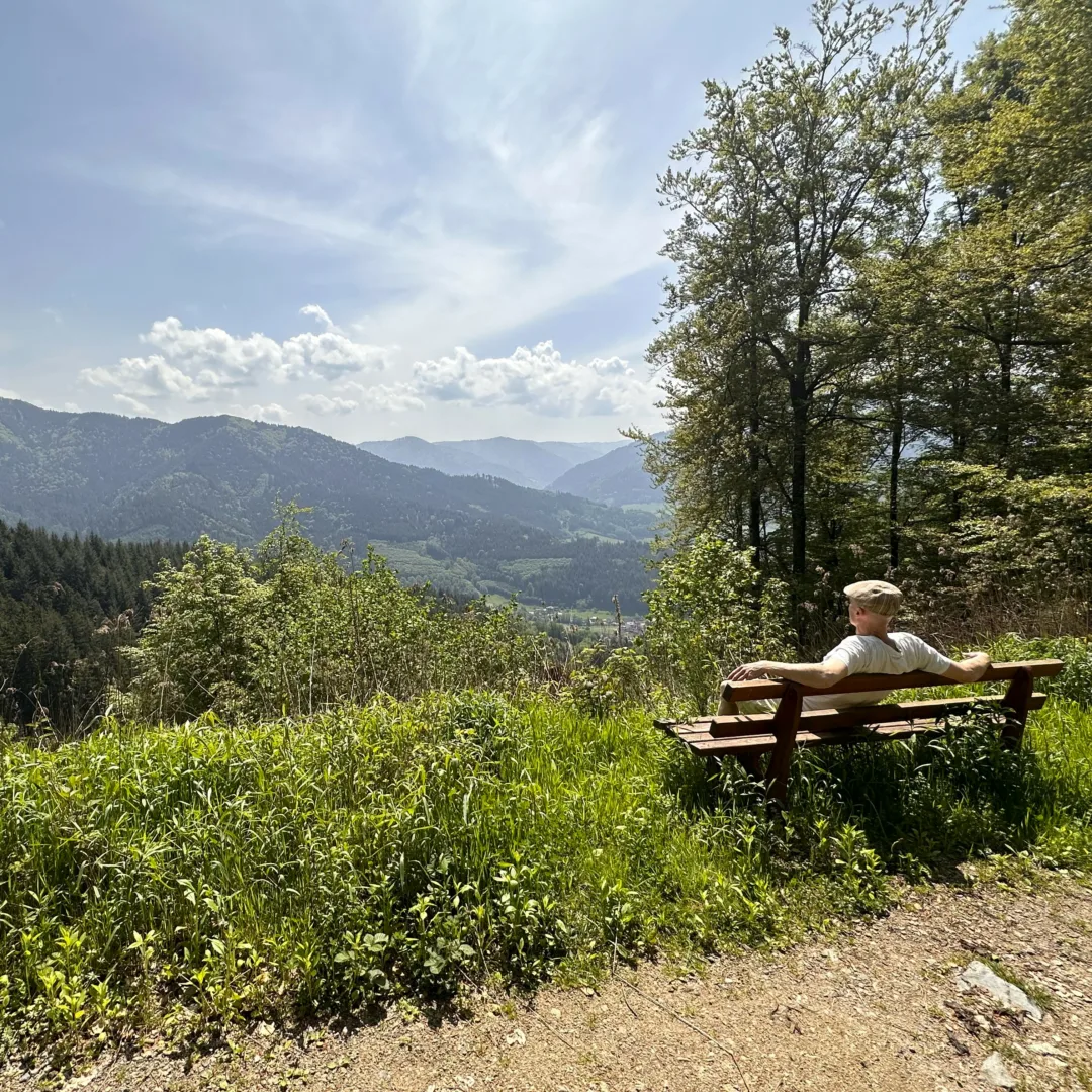 A man sitting on a bench in the sun, overlooking Simonswald Valley.