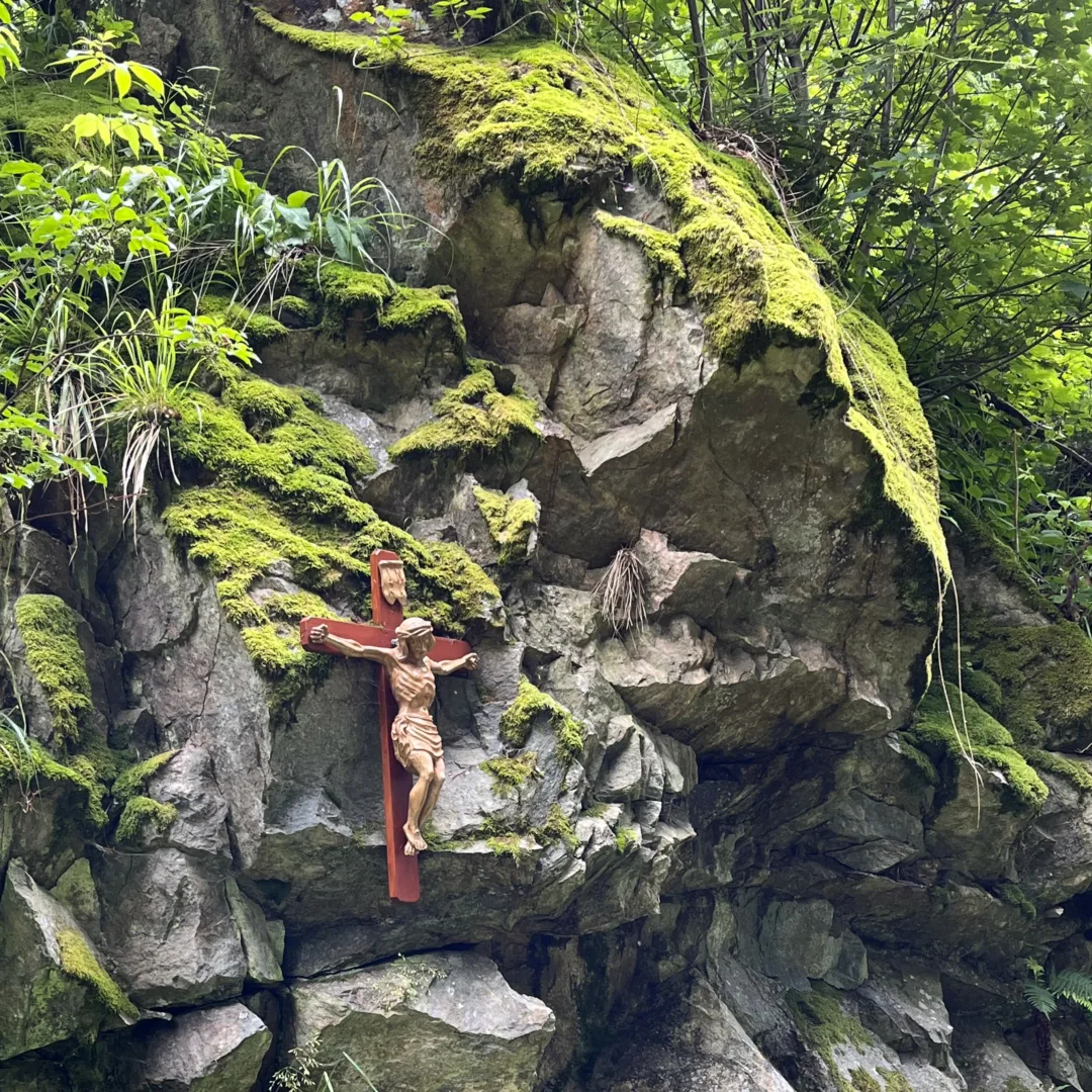 A devotional cross on a moss-covered rock wall along the path to the 'Our Lady' pilgrimage chapel.