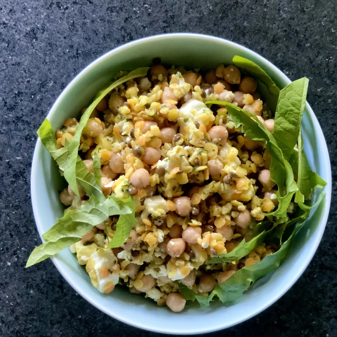 A bowl containing chickpeas, lentils, feta cheese, and fresh dandelion leaves.