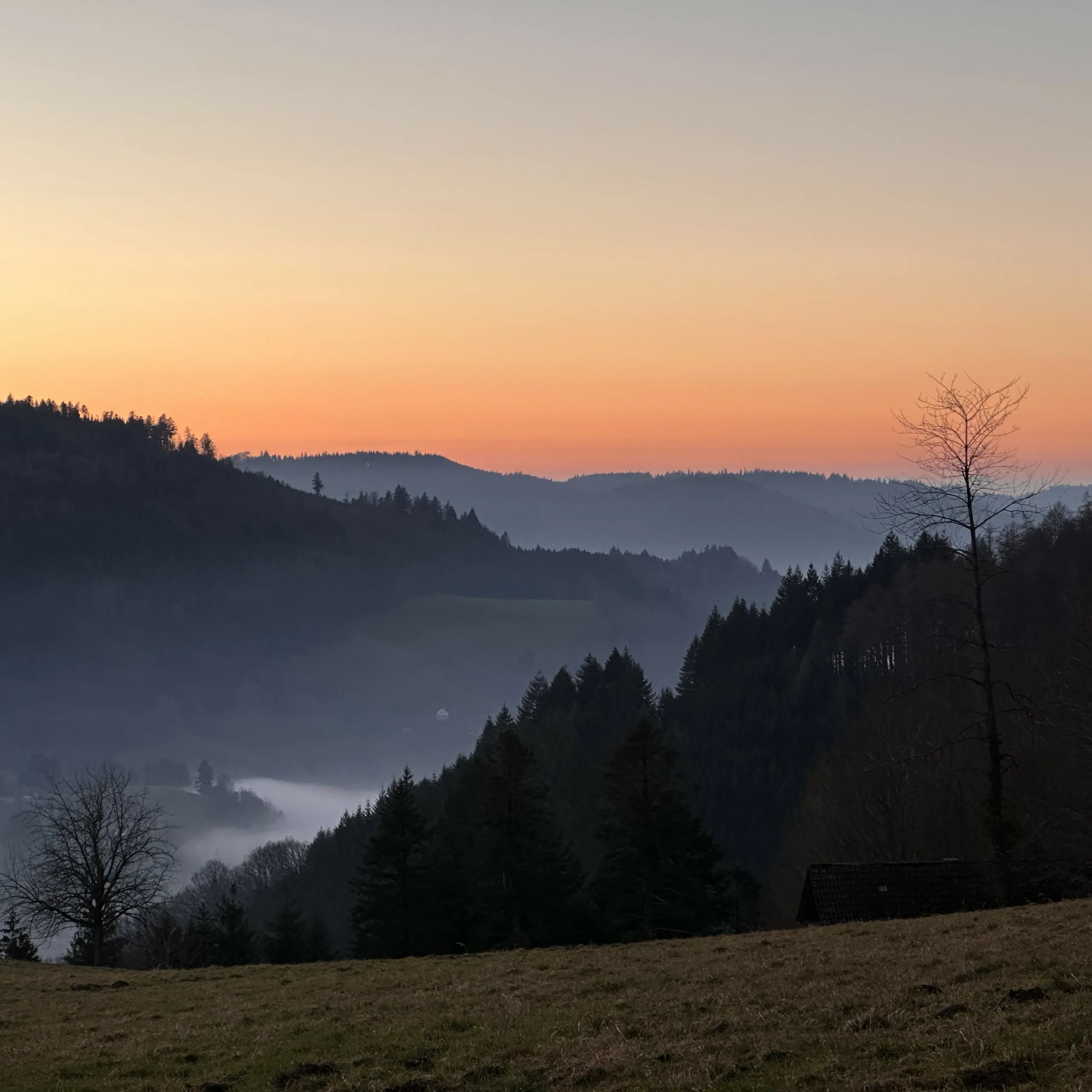 Eine Aussicht auf Berge, die atmosphärische Perspektive zeigen, vor einem lebhaft orangefarbenen Himmel.