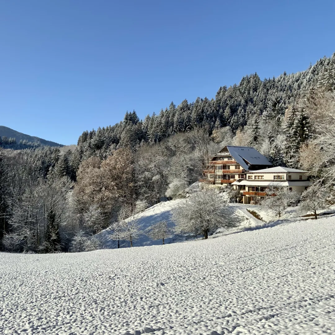 The retreat center nestled in a snowy landscape, with a clear blue sky above a forested mountain.