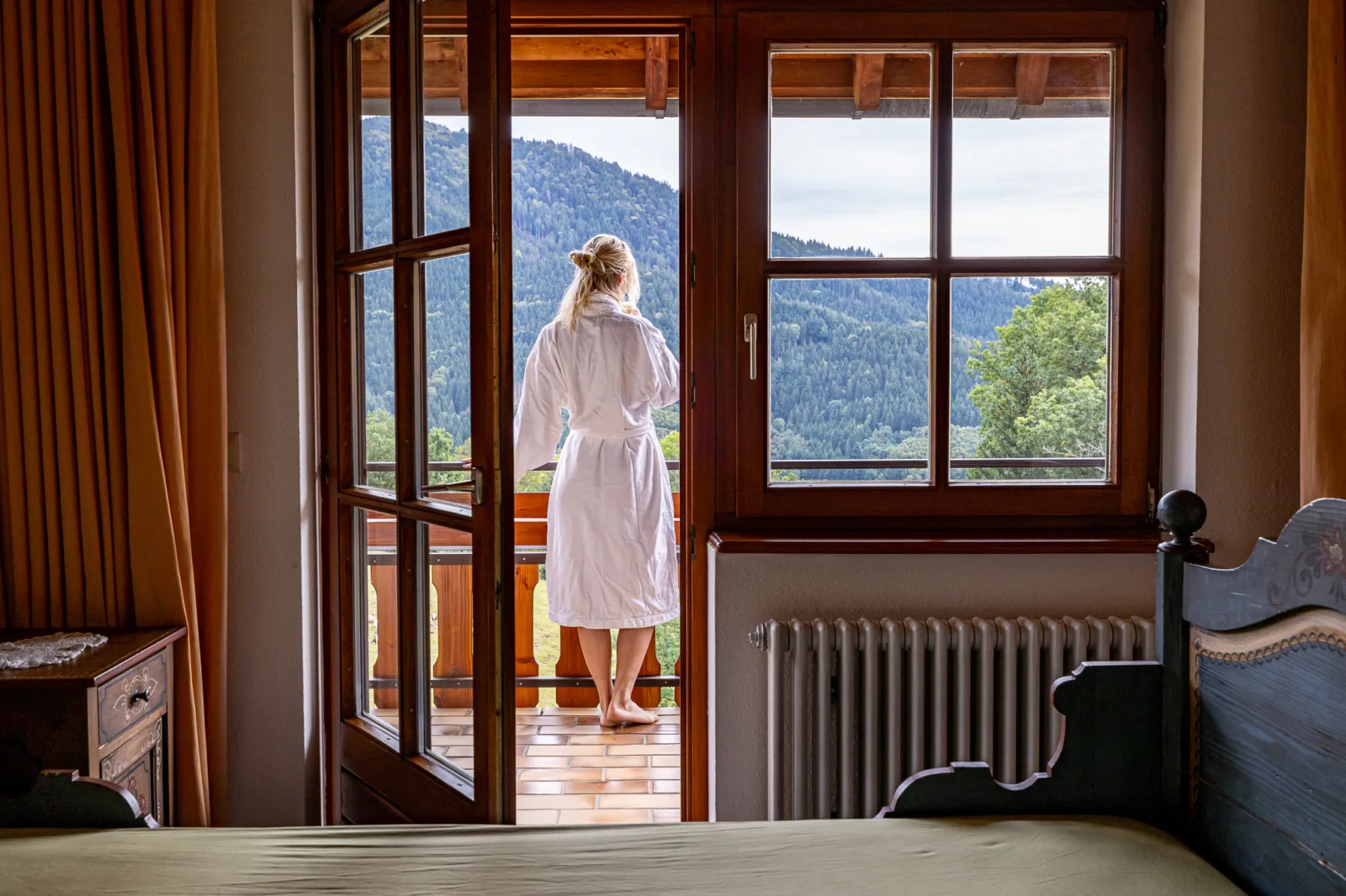 A woman standing on the balcony of a traditional valley-view room, enjoying the magnificant mountain view.