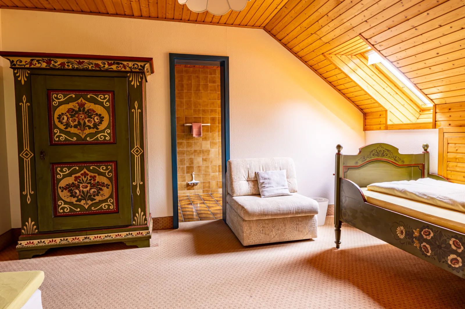 The cozy interior of a traditional forest-view room, featuring a single bed and additional wooden furniture painted with colorful details.