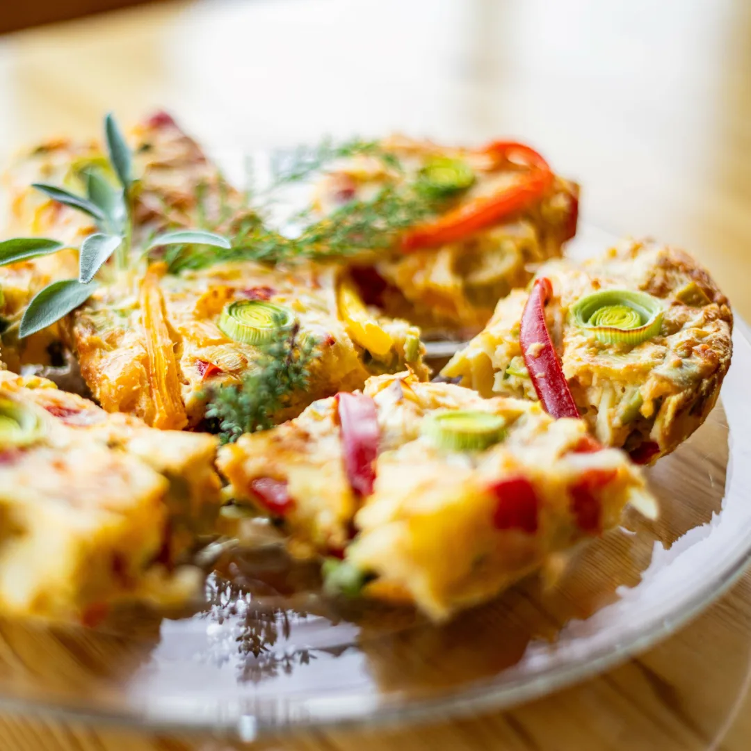 Squares of freshly baked vegetable pie with leeks and bell peppers, garnished with herbs.