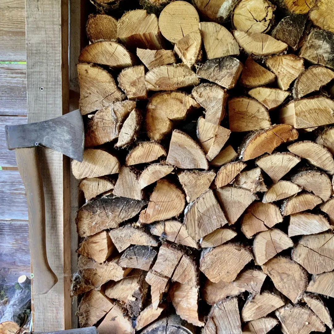 Cut firewood neatly stacked in a shed, with an axe hanging next to it.